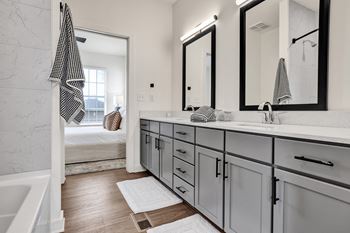Modern bathroom with white tub/shower combo, wood-designed flooring, and double vanity with framed mirrors.